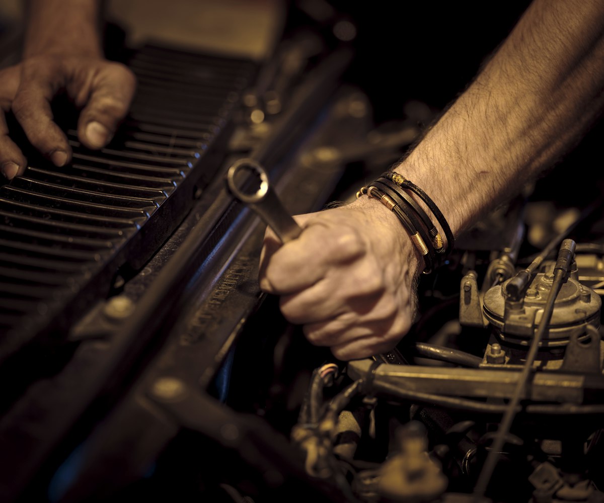 Two greased hands holding a spanner over an engine bay