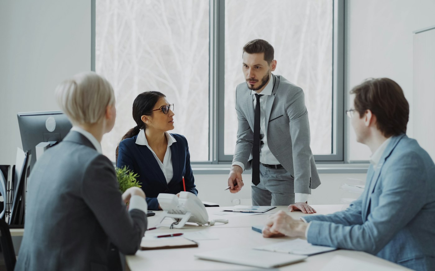 A sales manager standing at a boardroom table, talking through figures with three colleagues