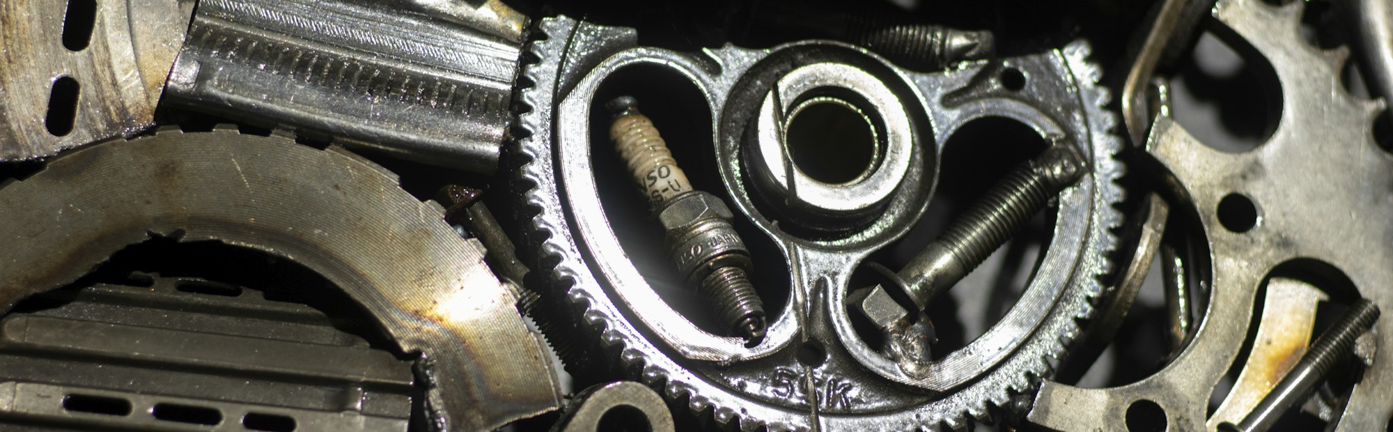 Close-up of oily gears, a timing chain and a spark plug inside a stripped engine